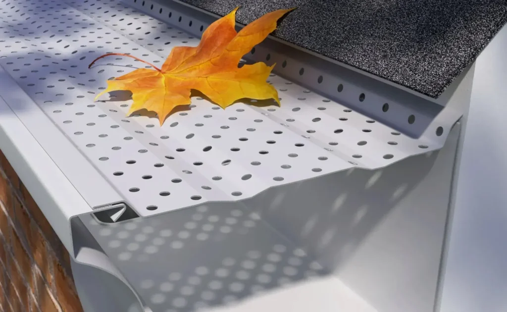 White perforated gutter guard with an autumn leaf below a roof edge